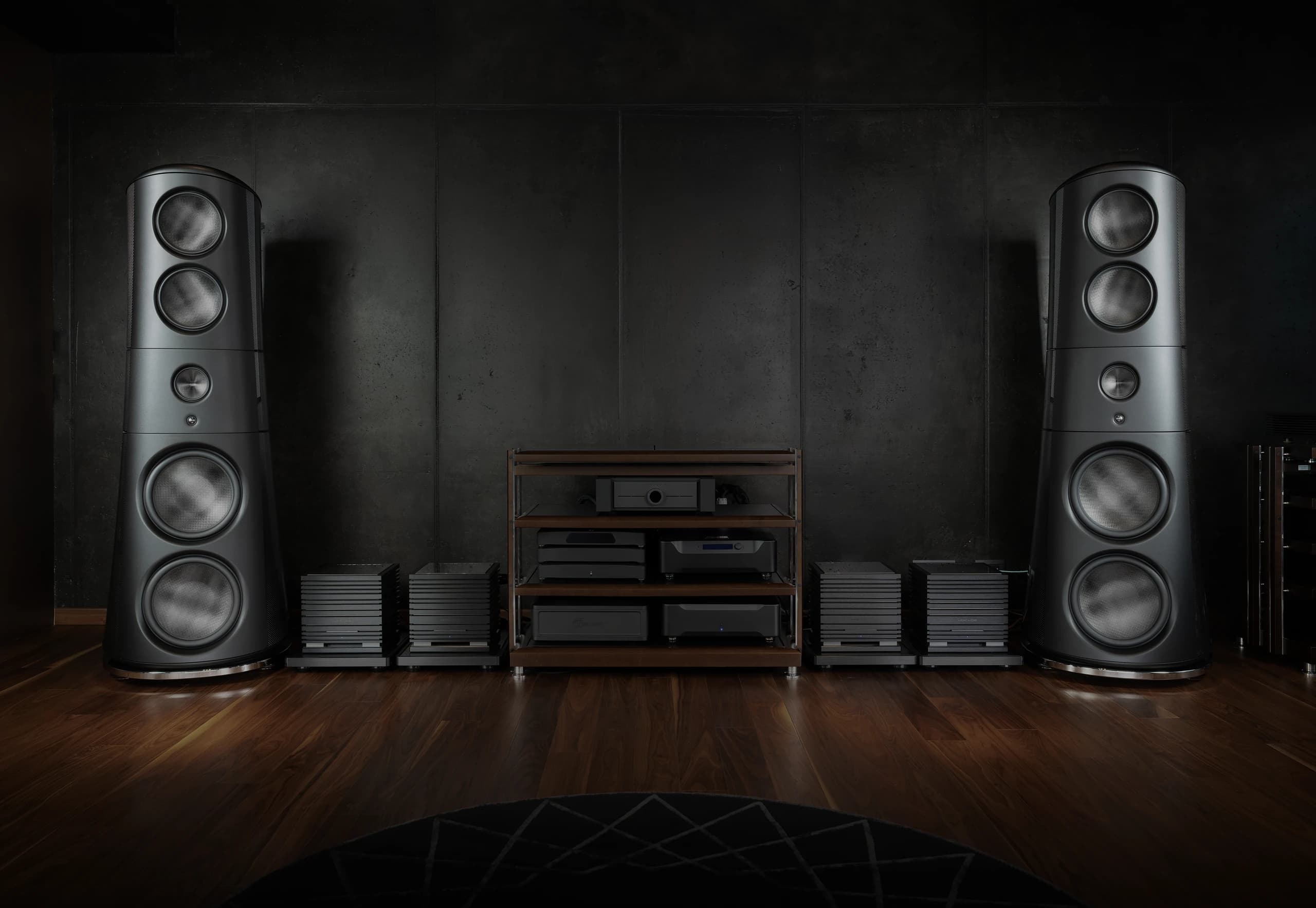 Listening room with two tall loudspeakers flanking an equipment rack and four UBICUBE amplifiers