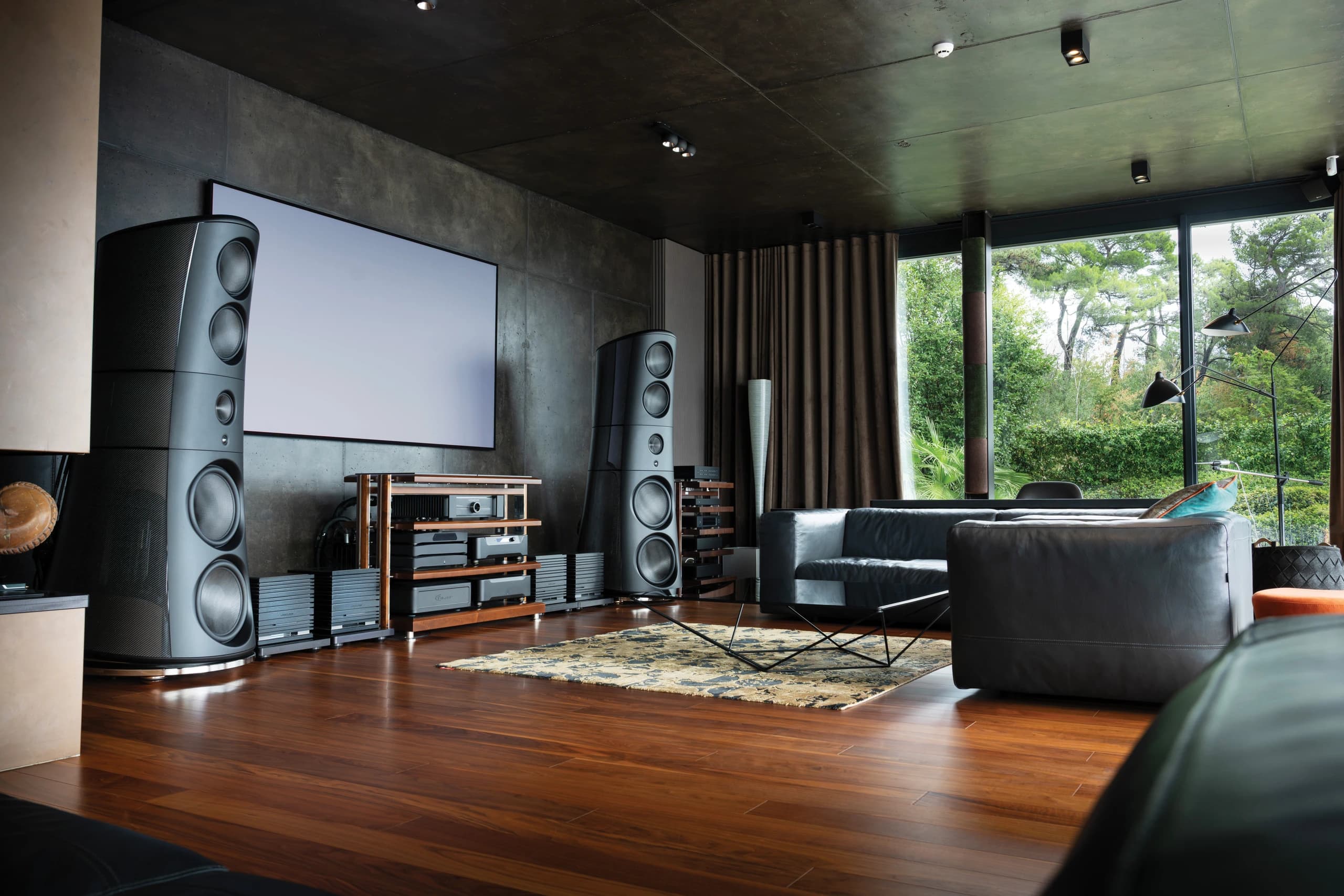 Listening room with two tall loudspeakers and a projection screen, UBICUBE amplifiers beside a wooden equipment rack