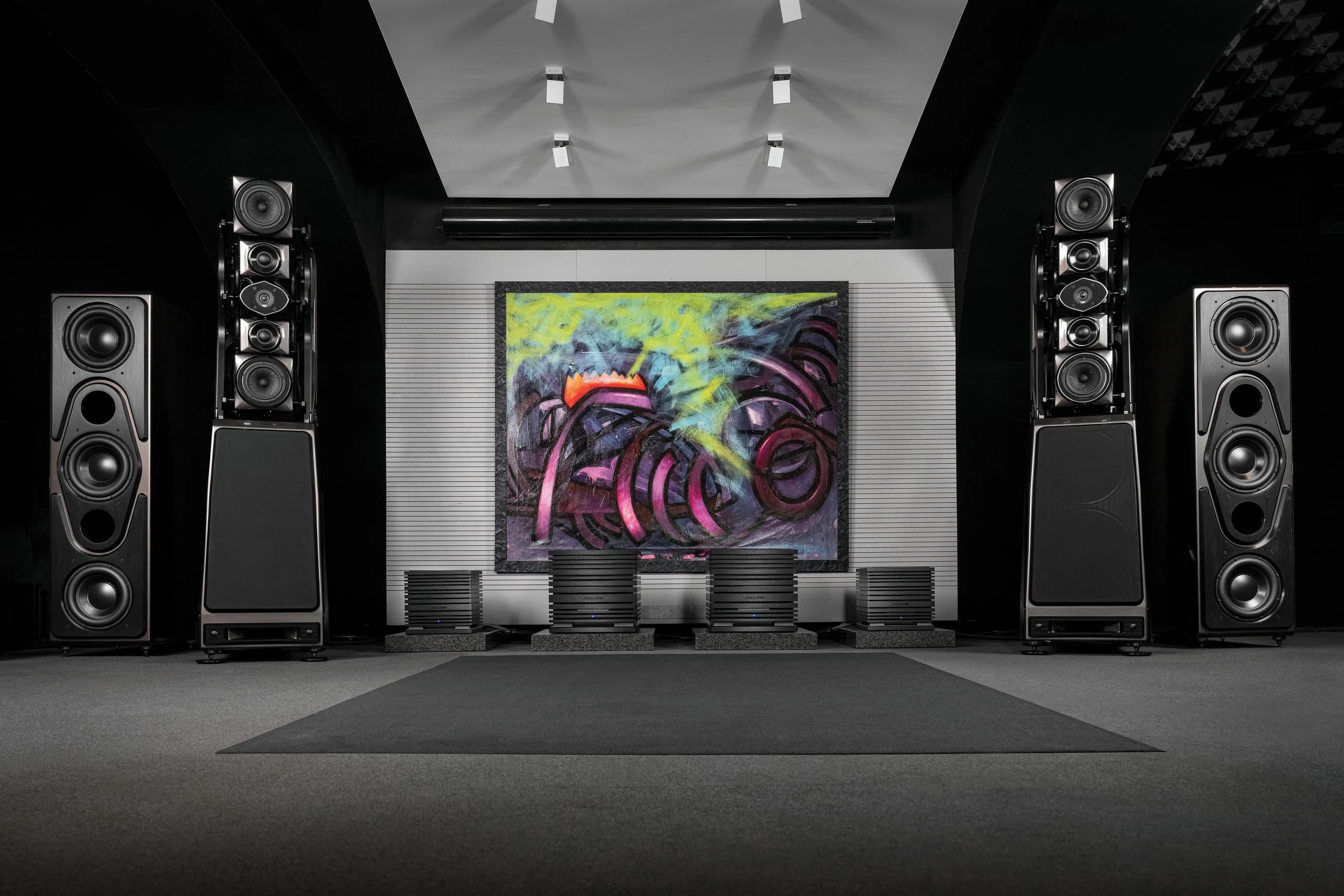 Listening room with large loudspeakers in front of a graffiti artwork and a row of UBICUBE amplifiers between them